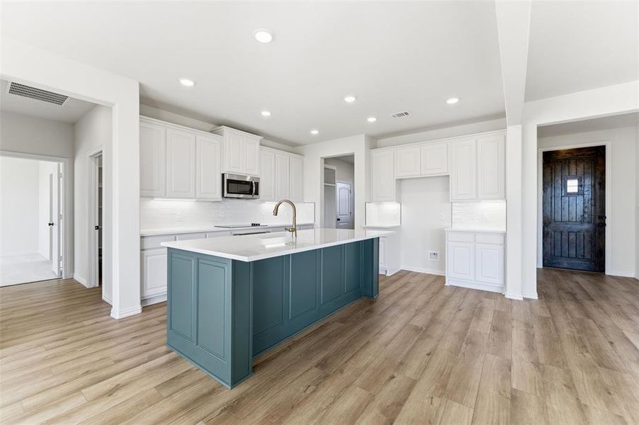 Kitchen featuring white cabinets, an island with sink, light wood-style flooring, recessed lighting, and stainless steel microwave