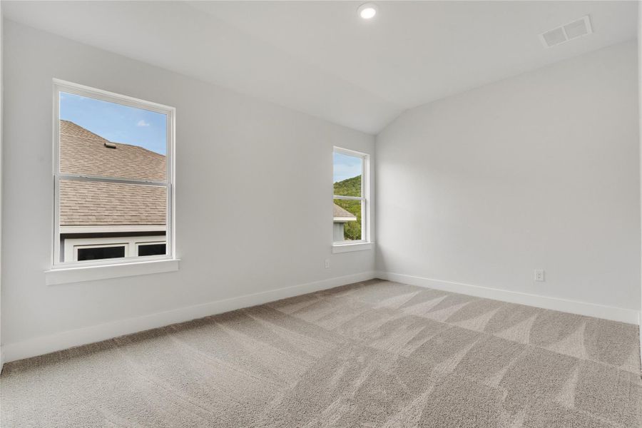 A spacious bedroom offers comfort with vaulted ceilings and abundant natural light from multiple windows.