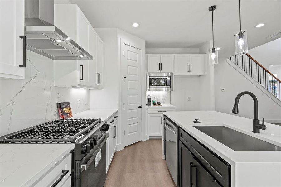 Kitchen with wall chimney exhaust hood, stainless steel appliances, sink, pendant lighting, and white cabinets