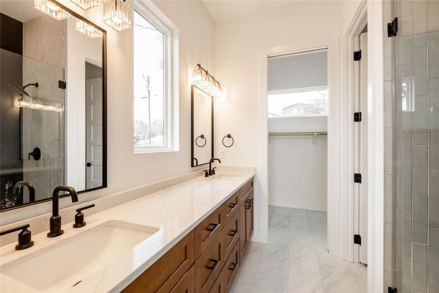 Full bathroom with double vanity, tiled shower, a walk in closet, and light marble finish flooring