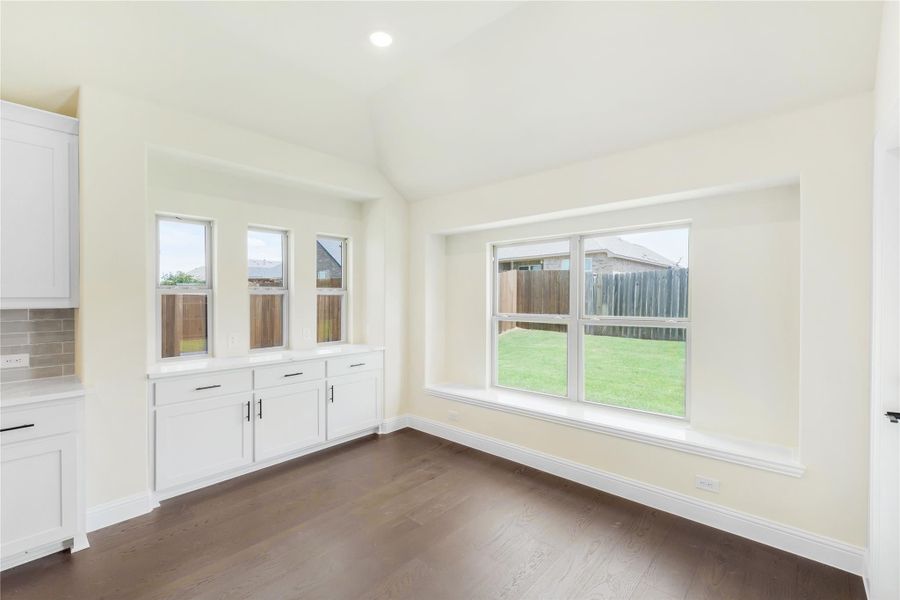 Bright dining area with dark hardwood floors, white built-in cabinets, and large windows overlooking a fenced backyard. Bright dining area with dark hardwood floors, white built-in cabinets, and large windows overlooking a fenced backyard.