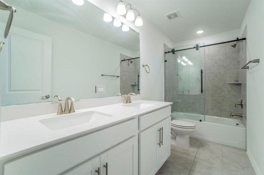 Bathroom featuring double vanity, shower / bath combination with glass door, light tile patterned floors, and recessed lighting Bathroom featuring double vanity, shower / bath combination with glass door, light tile patterned floors, and recessed lighting