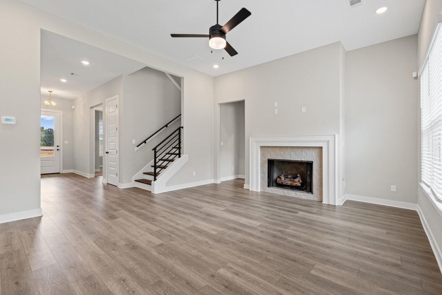 Spacious living area featuring wood-finish flooring, a fireplace with a stone surround and mantel, and recessed lighting Spacious living area featuring wood-finish flooring, a fireplace with a stone surround and mantel, and recessed lighting
