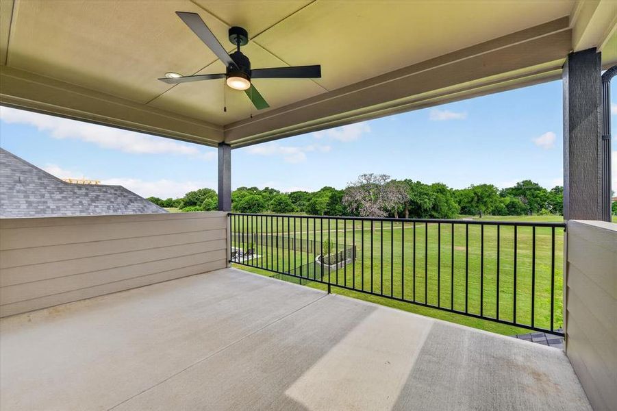 Covered balcony featuring a ceiling fan with integrated lighting, concrete flooring, and an open metal railing overlooking a landscaped green space