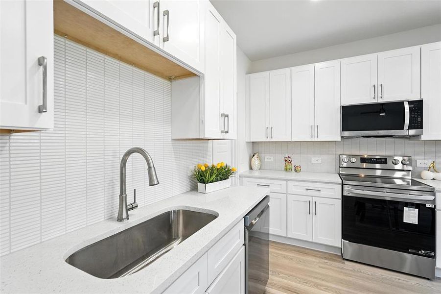 Kitchen with stainless steel appliances, tasteful backsplash, white cabinets, light wood-type flooring, and light stone counters