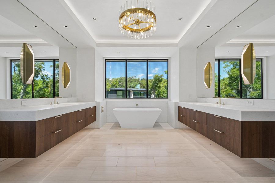Custom floating vanities frame a freestanding soaking tub under a tiered tray ceiling. Custom floating vanities frame a freestanding soaking tub under a tiered tray ceiling.