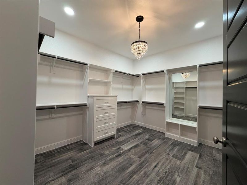 Walk-in closet featuring wood-finish flooring, custom shelving, integrated drawer storage, and a built-in dressing bench with mirror