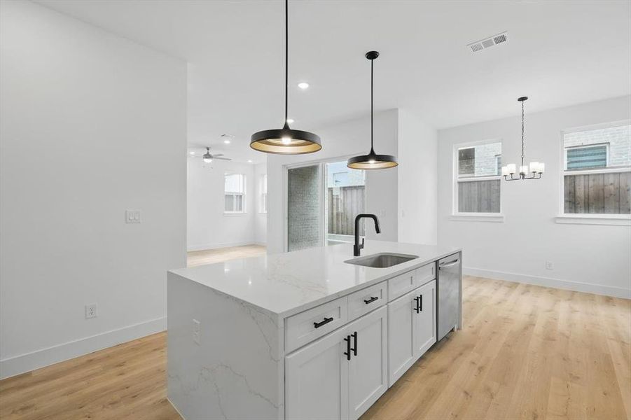 Kitchen featuring a sink, dishwasher, light wood finished floors, baseboards, and a chandelier