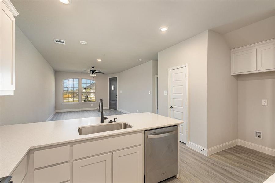 Kitchen with stainless steel dishwasher, sink, white cabinets, and ceiling fan