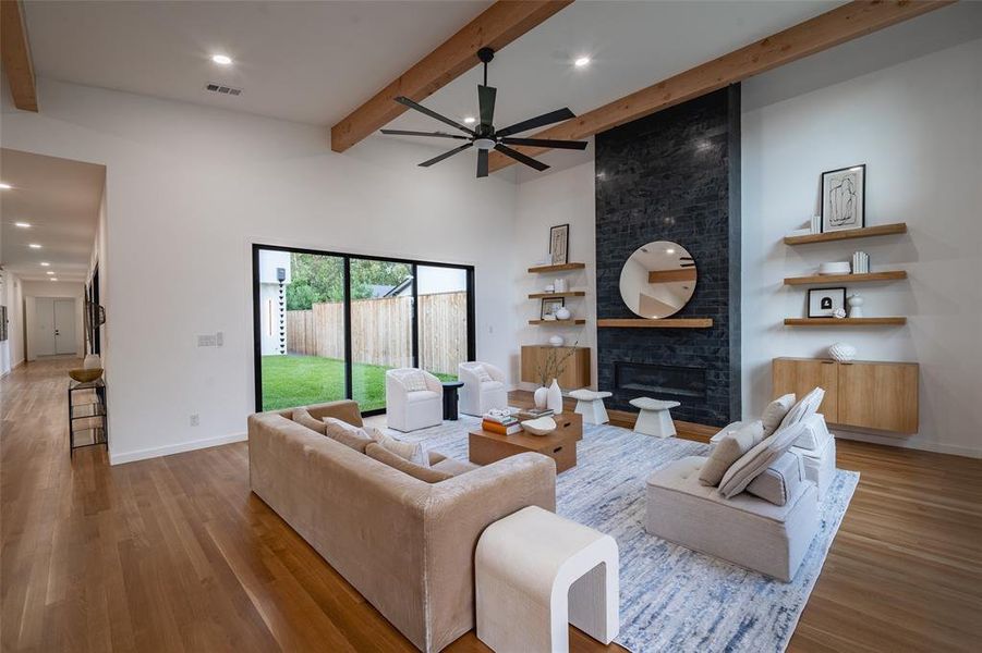 Living room with ceiling fan, beamed ceiling, a brick fireplace, light hardwood / wood-style flooring, and a towering ceiling