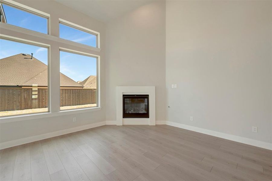 Unfurnished living room featuring a glass covered fireplace, light wood-style flooring, and a high ceiling