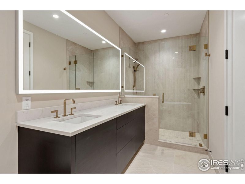 The primary ensuite includes a ton of counter space, a large walk-in shower with three shower heads, a beautiful back-lit mirror and a 59 inch soaker tub (seen in the next photo).