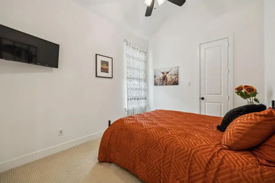 Bedroom featuring light colored carpet, lofted ceiling, baseboards, and a ceiling fan