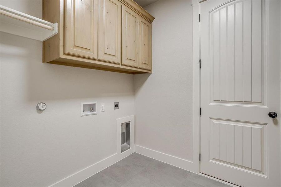 Clothes washing area with cabinets, electric dryer hookup, hookup for a gas dryer, hookup for a washing machine, and light tile patterned floors