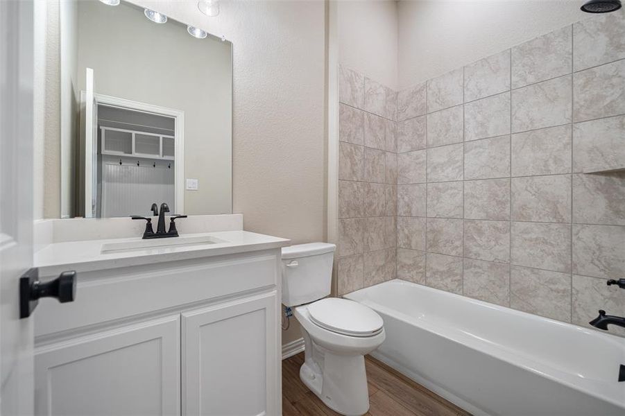 Bathroom with dark wood finished floors, bathing tub / shower combination, vanity, and a textured wall