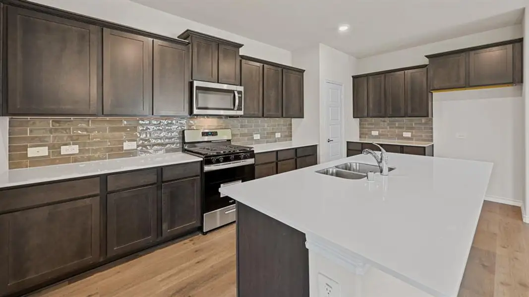 Contemporary kitchen featuring an expansive island with a double basin sink, dark wood cabinetry, white countertops, and a subway tile backsplash Contemporary kitchen featuring an expansive island with a double basin sink, dark wood cabinetry, white countertops, and a subway tile backsplash