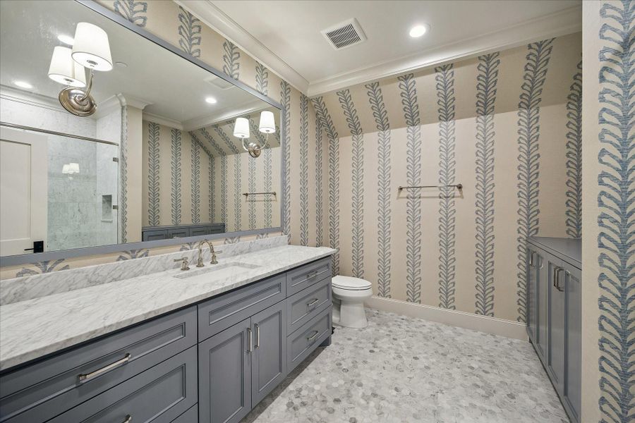 Beautifully designed secondary bath up featuring a marble slab countertop, custom painted cabinetry, and a sleek undermount sink paired with polished fixtures. Designer wallpaper adds a beautiful look, while the mosaic tile flooring brings subtle texture and visual interest. Thoughtfully finished with crown molding and quality detailing throughout, creating a stylish and functional space.