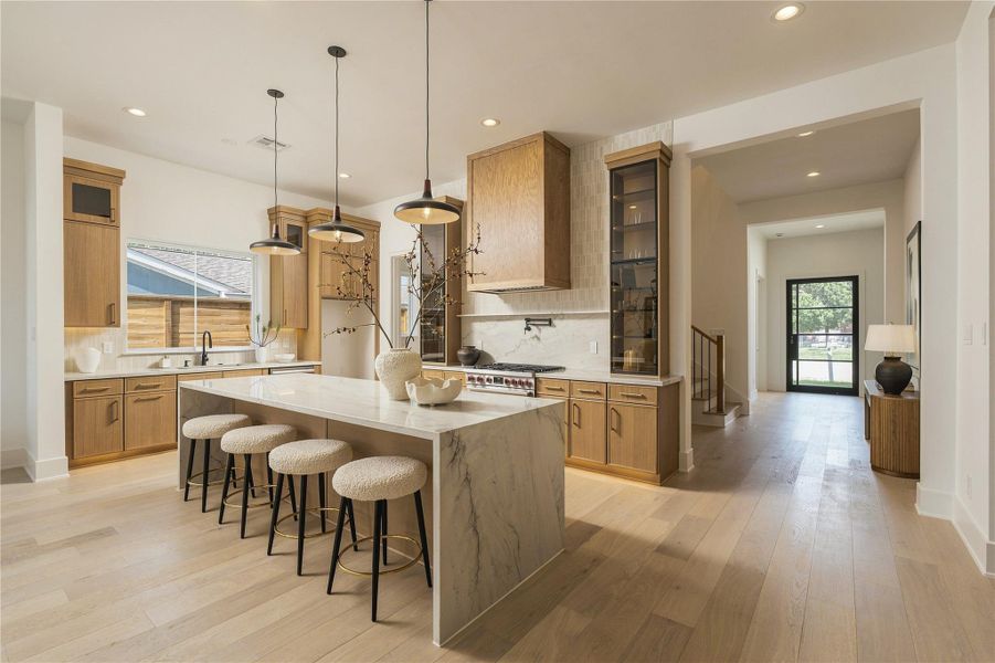 The kitchen makes an immediate statement with imported Mount Blanc Quartzite, custom cabinetry, and a dramatic oversized island, creating a natural centerpiece for both everyday living and entertaining.