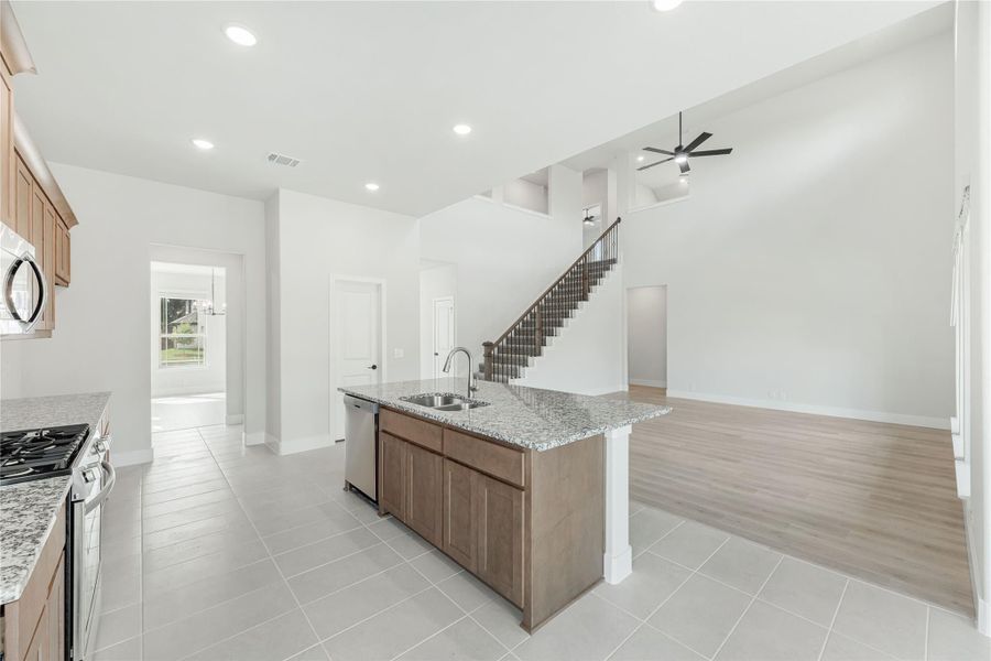 Kitchen island with granite countertop and sink, open to living area with staircase and ceiling fan