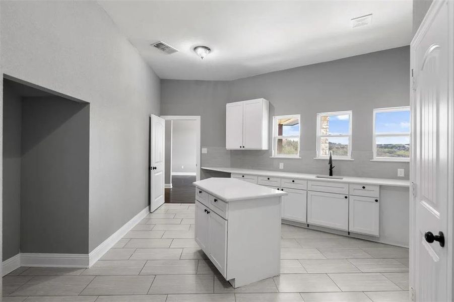 Kitchen featuring white cabinets, light countertops, a center island, and backsplash