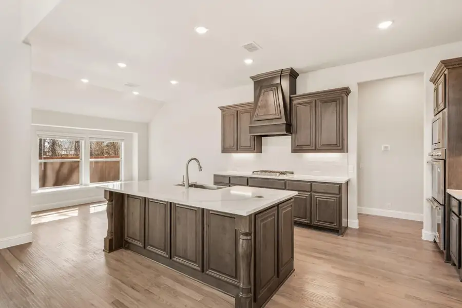 Kitchen with dark wood cabinets, large center island with sink, custom range hood, and hardwood floors