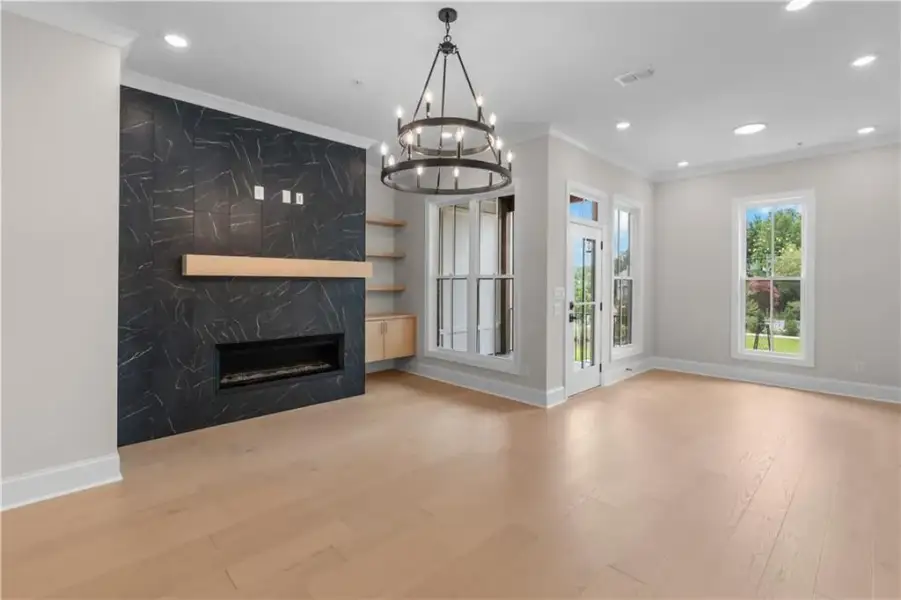 Light wood-finish flooring, recessed lighting, and a linear fireplace with a dark stone-look surround