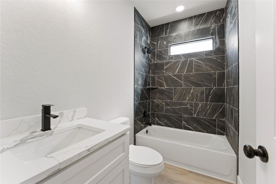 Full bath featuring vanity, bathing tub / shower combination, light wood-style flooring, and a textured wall