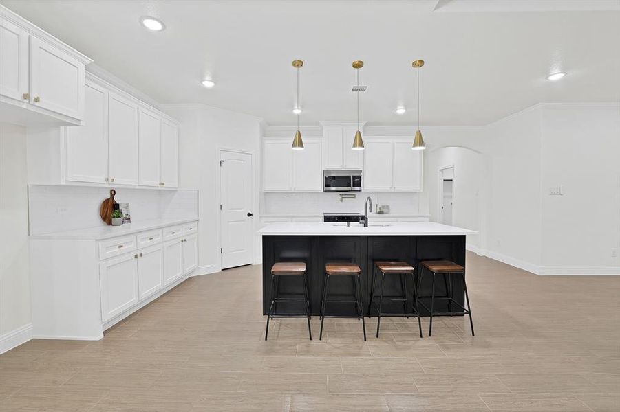 Kitchen with a center island with sink, sink, hanging light fixtures, light wood-type flooring, and white cabinetry