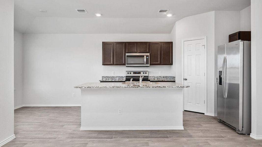 Kitchen with stainless steel appliances, dark brown cabinetry, light stone counters, light wood finished floors, and recessed lighting