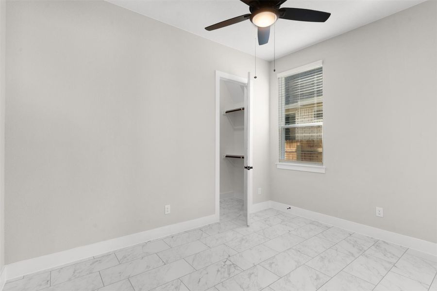 Unfurnished bedroom with a spacious closet, a ceiling fan, and light marble finish floors