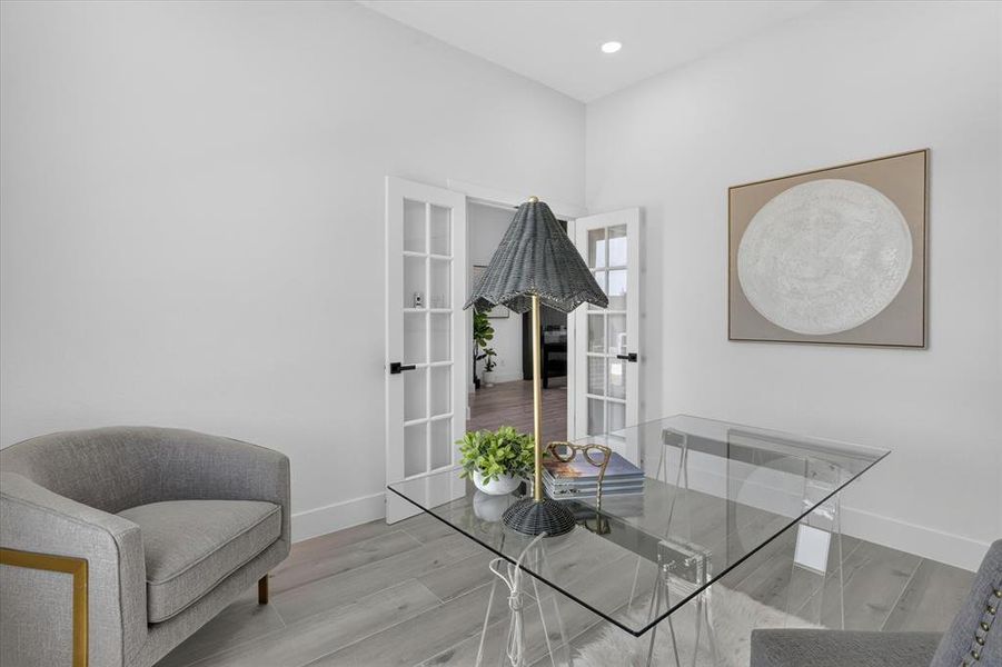 Spacious room featuring light wood-finish flooring, white walls, and elegant French doors with black hardware