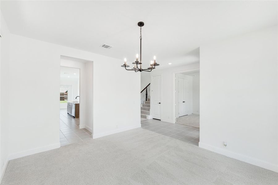 Empty dining room with black chandelier, light carpet, and open view to kitchen and staircase