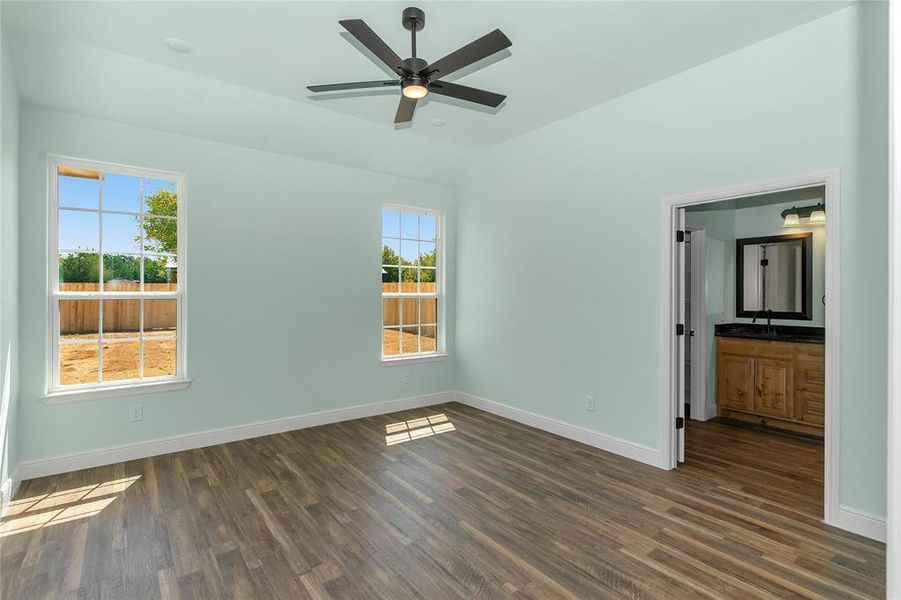 Unfurnished bedroom featuring lofted ceiling, multiple windows, dark wood finished floors, and connected bathroom