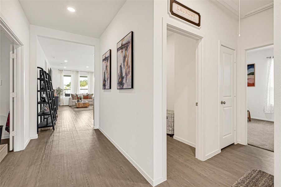 Bright and inviting hallway with wood flooring leads to a cozy living area, featuring stylish wall art and convenient access to a laundry room and additional spaces. Bright and inviting hallway with wood flooring leads to a cozy living area, featuring stylish wall art and convenient access to a laundry room and additional spaces.