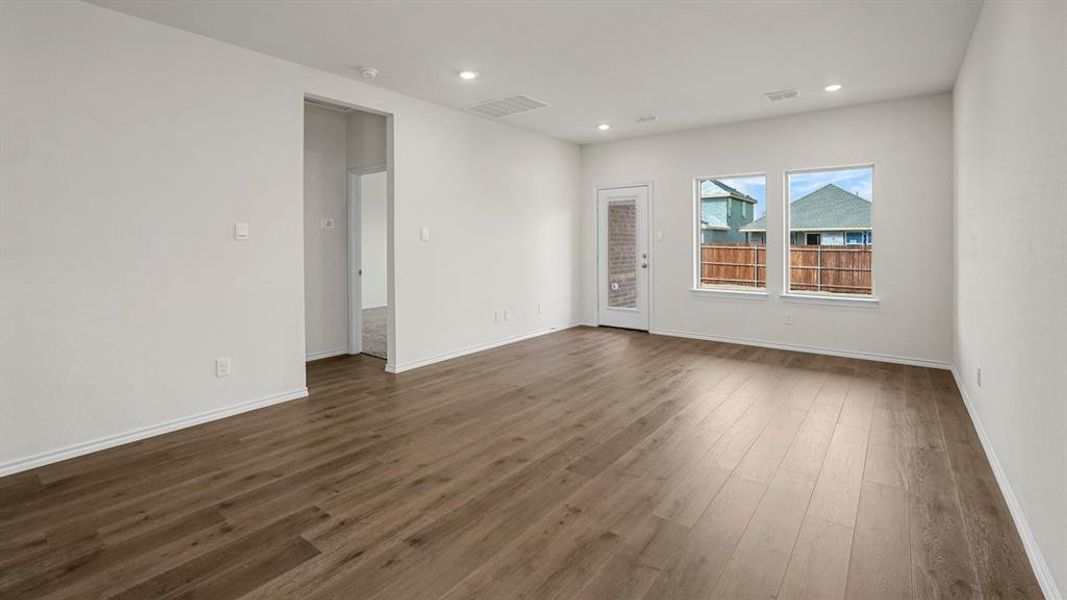Spacious living area featuring hard surface flooring, white walls, recessed lighting, and a glass-paneled door leading to the exterior