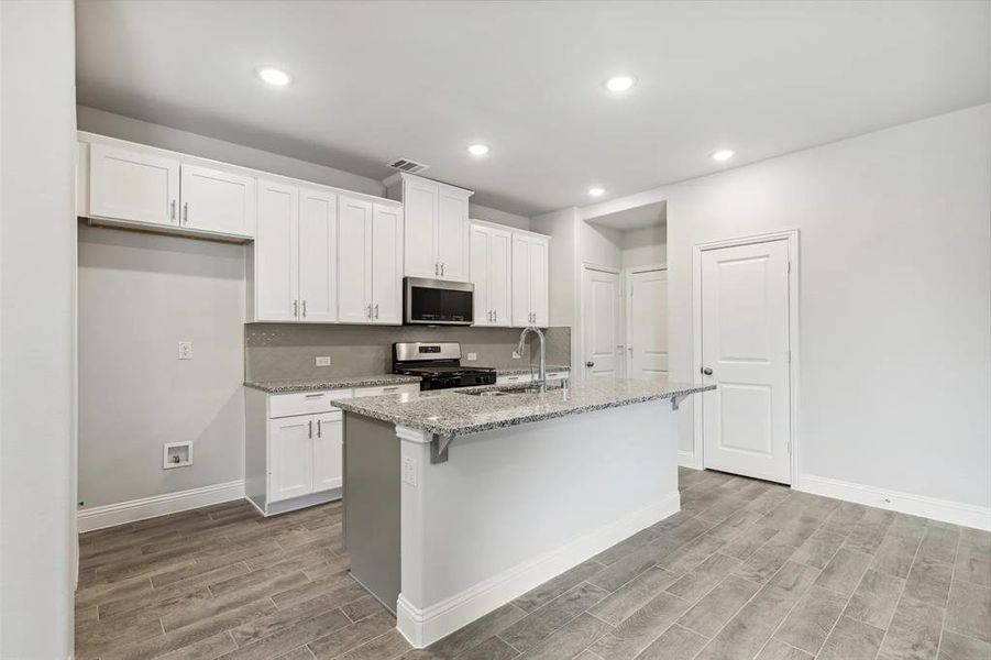 Kitchen with a center island with sink, white cabinets, sink, light stone countertops, and appliances with stainless steel finishes