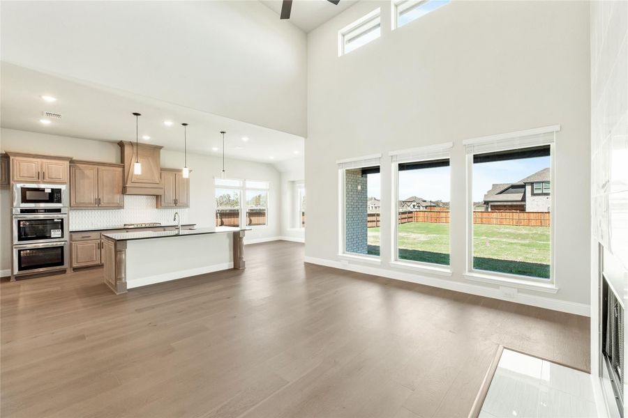 Open-concept living area with hardwood floors, high ceilings, and kitchen with island and wood cabinets visible in background Open-concept living area with hardwood floors, high ceilings, and kitchen with island and wood cabinets visible in background
