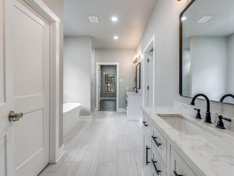 Bathroom featuring two vanities, a soaking tub, and recessed lighting