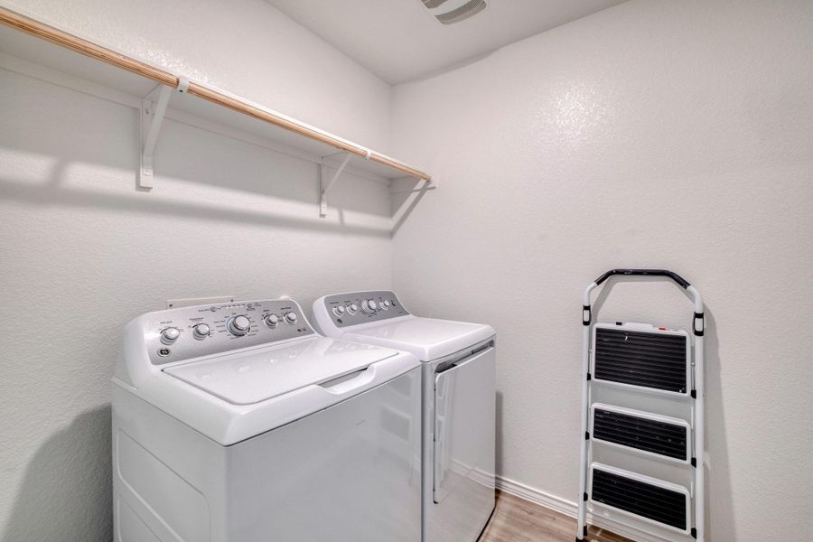 Dedicated laundry area featuring a wall-mounted wooden hanging rod, white shelving brackets, and wood-finish flooring