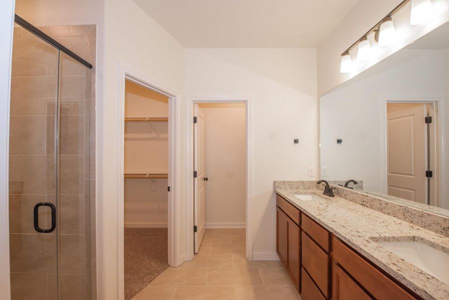 Bathroom featuring double vanity, light tile patterned floors, a stall shower, and a walk in closet
