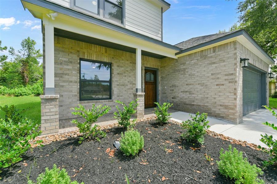 You're looking at the front exterior,  featuring large windows, and a covered entryway. The property includes newly landscaped beds with shrubs and a well-maintained lawn.