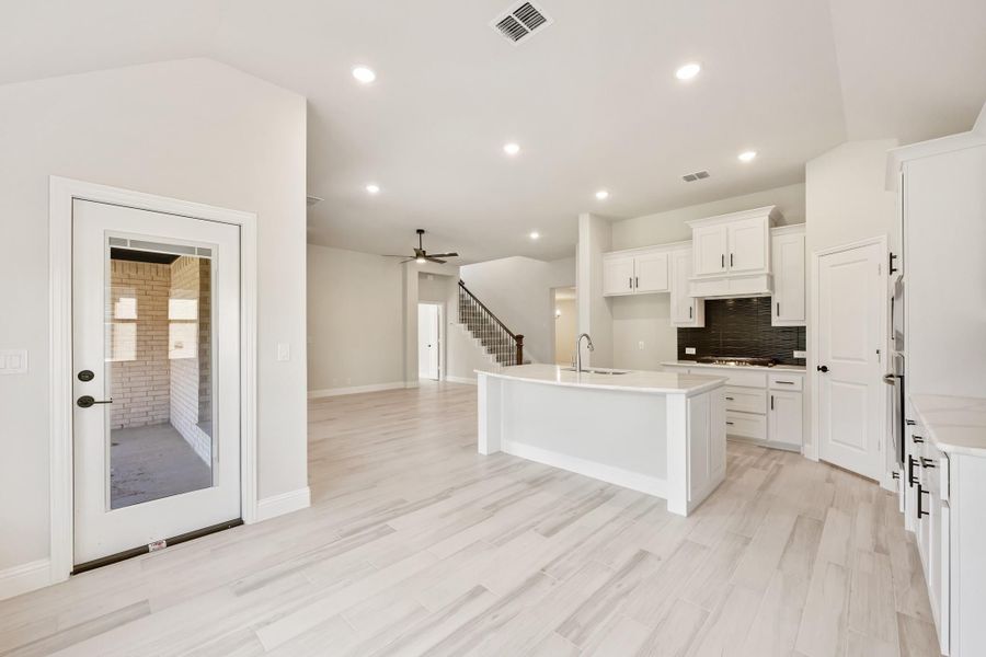 Open kitchen and living area with white cabinets, center island, dark tile backsplash, and light wood floors Open kitchen and living area with white cabinets, center island, dark tile backsplash, and light wood floors