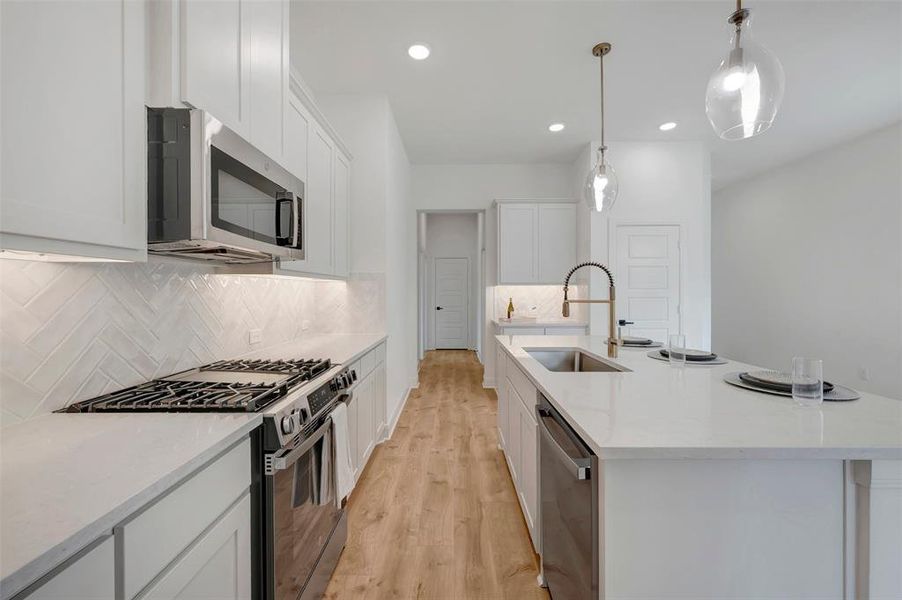 Modern kitchen featuring white shaker cabinetry, stainless steel appliances, a herringbone tile backsplash, and a large island with a sink and pendant lighting