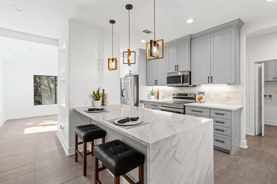 Kitchen with a kitchen breakfast bar, a peninsula, appliances with stainless steel finishes, light stone counters, and hanging light fixtures