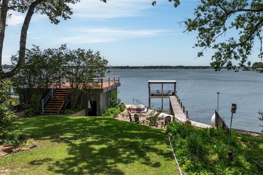 Waterfront property featuring a private boat dock with covered seating, a multi-level deck, and a manicured lawn