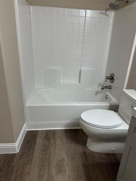 Bathroom with toilet, wood finished floors, baseboards, and bathtub / shower combination