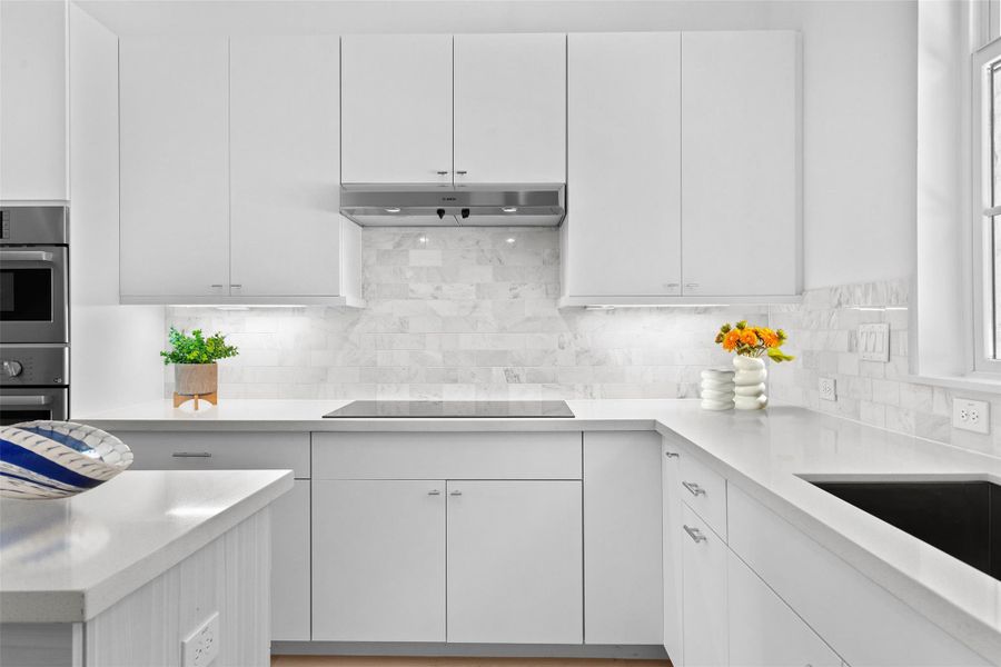 Kitchen featuring white cabinetry, backsplash, light stone countertops, and double oven