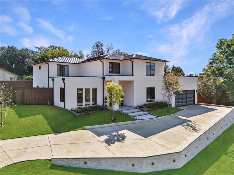View of front of property with concrete driveway, a front lawn, stucco siding, a metal roof, and a standing seam roof