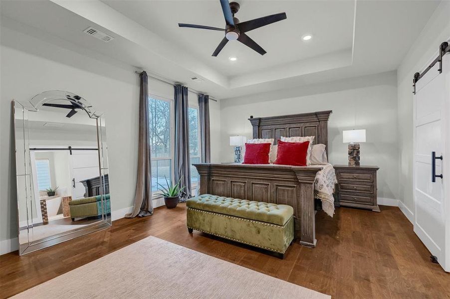 Bedroom with ceiling fan, a tray ceiling, dark hardwood / wood-style flooring, and a barn door