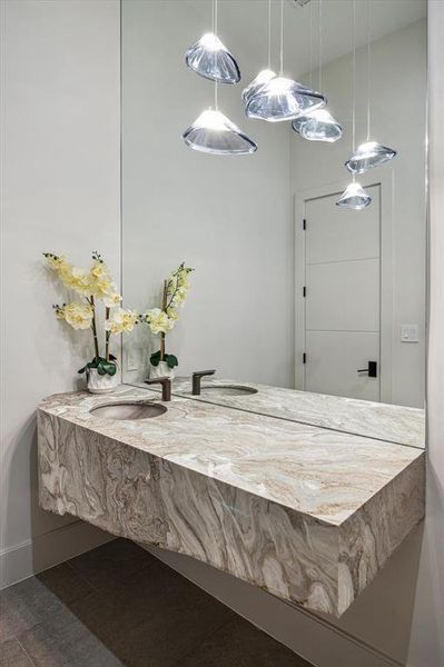 The formal powder room, located near the kitchen, features Dune Carved Natural floor tile, complemented by a NativeStone oval under-mount bathroom sink and Avalanche polished countertops. It includes a DXV one-piece toilet, recessed LED lighting, and designer neutral wall paint, creating a stylish and functional space for guests.